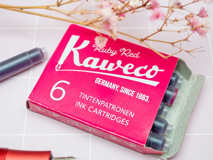 Eine Packung mit roten Tintenpatronen von Kaweco liegt auf einem hellrosa Untergrund. Foto: Johanna Rundel