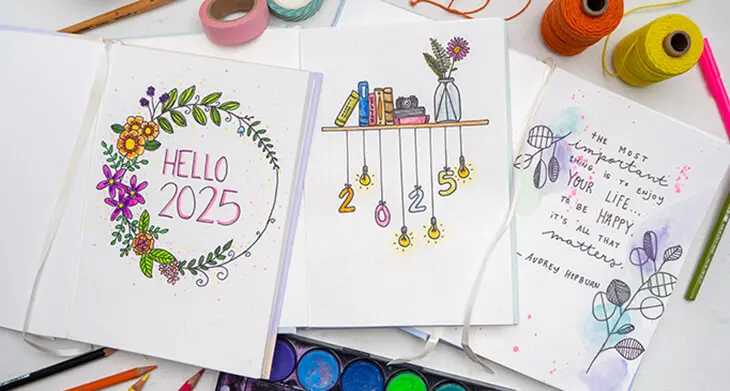 Drei Bullet Journals von Rössler liegen aufgeschlagen auf einem hellen Untergrund. Es sind die Deckblätter mit gestaltetem Design zum Jahreswechsel zu sehen. Foto: Johanna Rundel