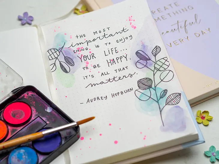Ein auf geschlagenes Bullet Journal von Rössler, auf dem Deckblatt ist ein Zitat von Audrey Hepburn geschrieben. Der Rest der Seite wurde mit Wasserfarben verschönert. Foto: Johanna Rundel