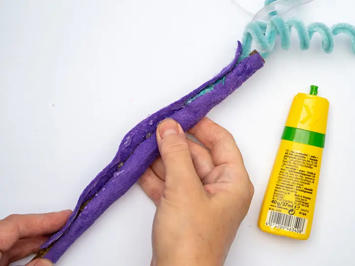 Jemand umklebt einen Stock mit einem Stück violettem Bastelfilz von KNORR prandell. Foto: Johanna Rundel