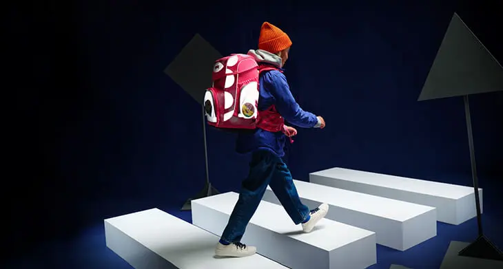 Ein Kind läuft mit einem reflektierenden Schulranzen von ergobag durch eine imaginäre Verkehrsszene