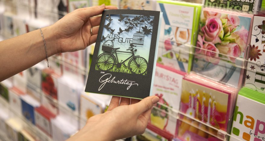 Eine Geburtstagskarten wird vor einer Wand mit weiteren Karten präsentiert.