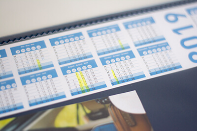 Detailaufnahme eines Kalenders, der sich unter der Folie einer Schreibtischunterlage befindet. 