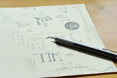 Auf einem Blatt ist der Name "Tim" in unterschiedlichen Varianten gelettert. Darauf liegt ein Stift der Marke Rotring. 