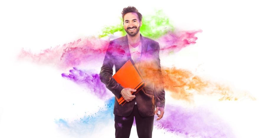 Ein Mann mit einer Ordungsmappe unter dem Arm wird mit Pulver in den Farben lila, orange, blau und grün beworfen.