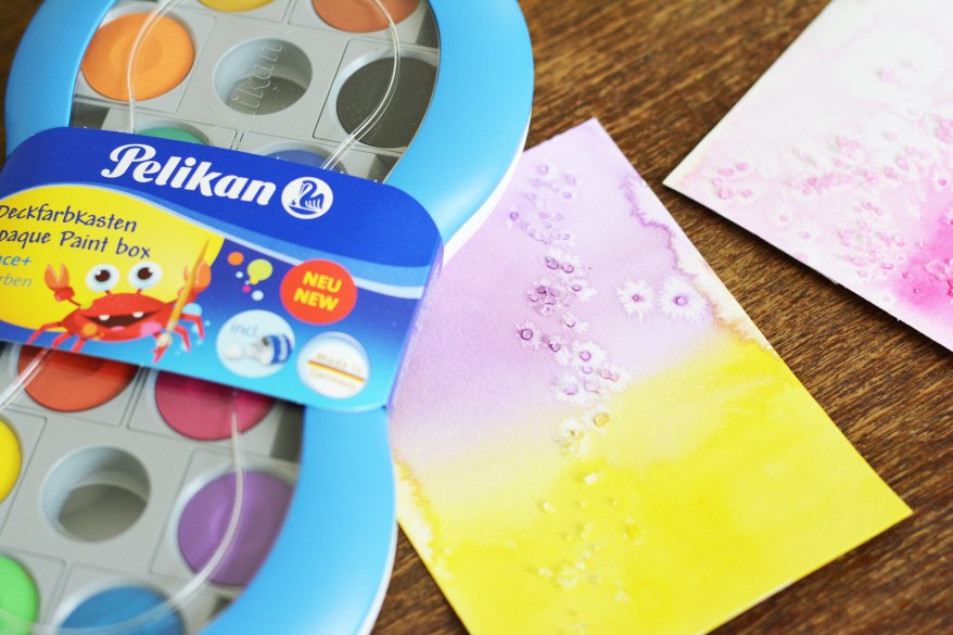 Pelikan Wassermalkasten, daneben eine Karte in lila und gelb mit Farbverläufen
