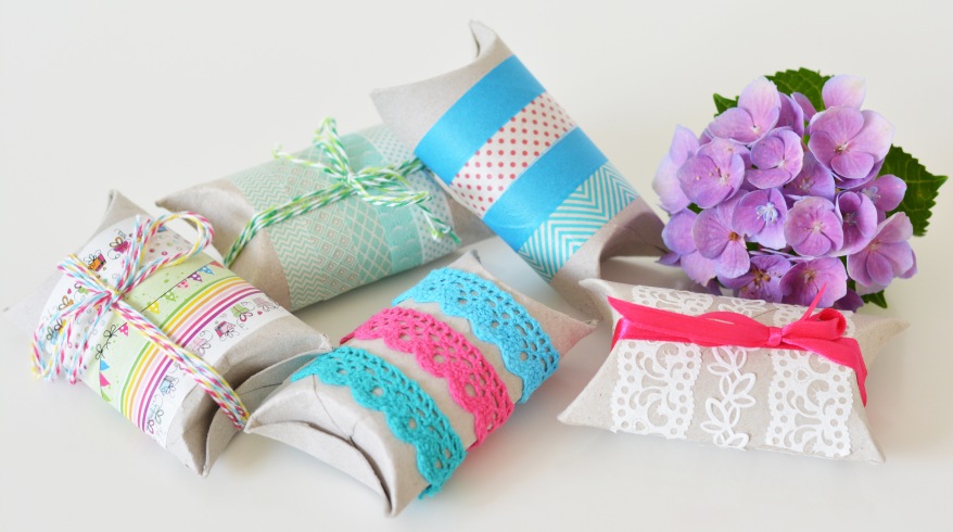 Mehrere Geschenkboxen aus Klopapierrollen, die mit Bändern verziert wurden. Im Hintergrund ist eine Blume zu sehen