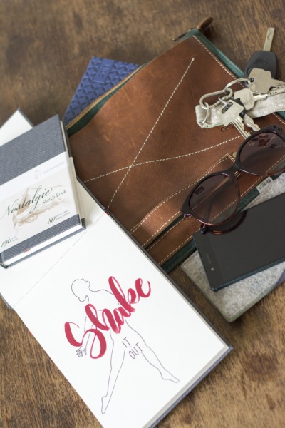 Lettering im Skizzenbuch neben Tasche, Handy, Schlüssel und Brille