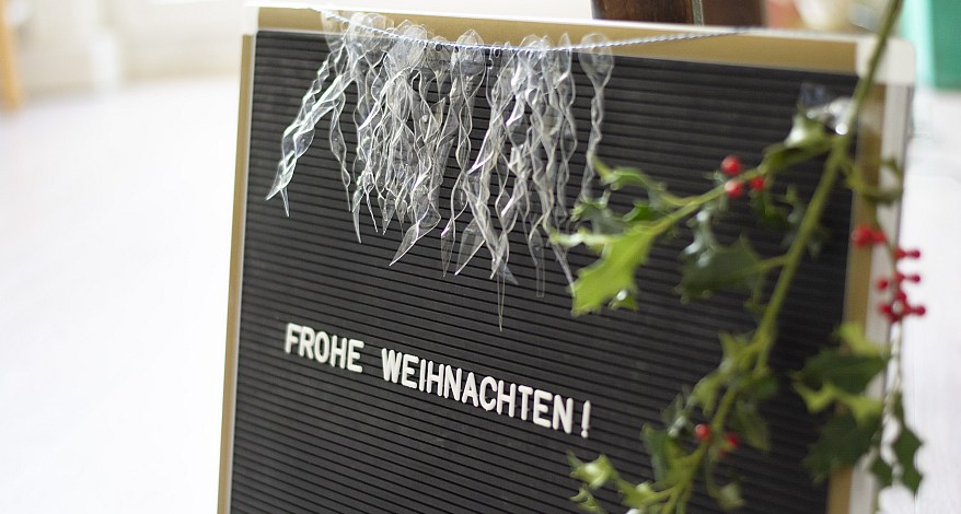 Schwarzes Letterboard mit „Frohe Weihnachten!“ und DIY-Eiszapfen aus Plastik.