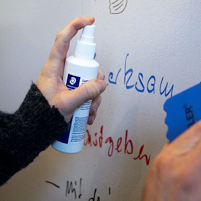 Nahaufnahme: Hand hält Flasche mit Reinungsmittel und sprüht an eine Wand.