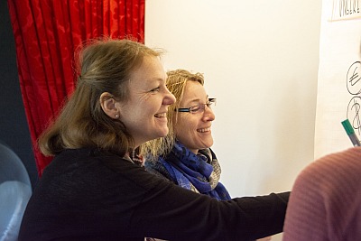 Mitarbeiter stehen am Flipchart und lachen.