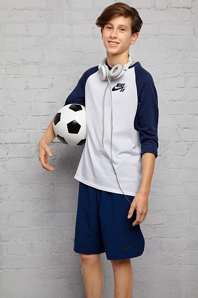 Junge in Sportkleidung hält einen Fußball und trägt Kopfhörer um den Hals.