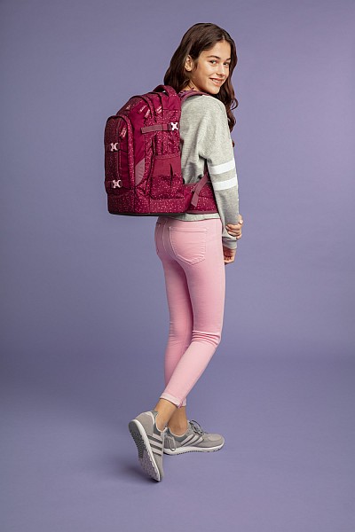 Mädchen mit pinker Jeans trägt einen pinken satch-Rucksack und schaut über die Schulter.