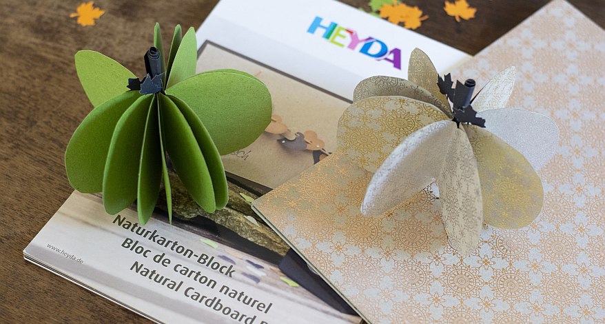 Gebastelte Kürbisse aus Papier liegen auf einer Verpackung der Marke Heyda.