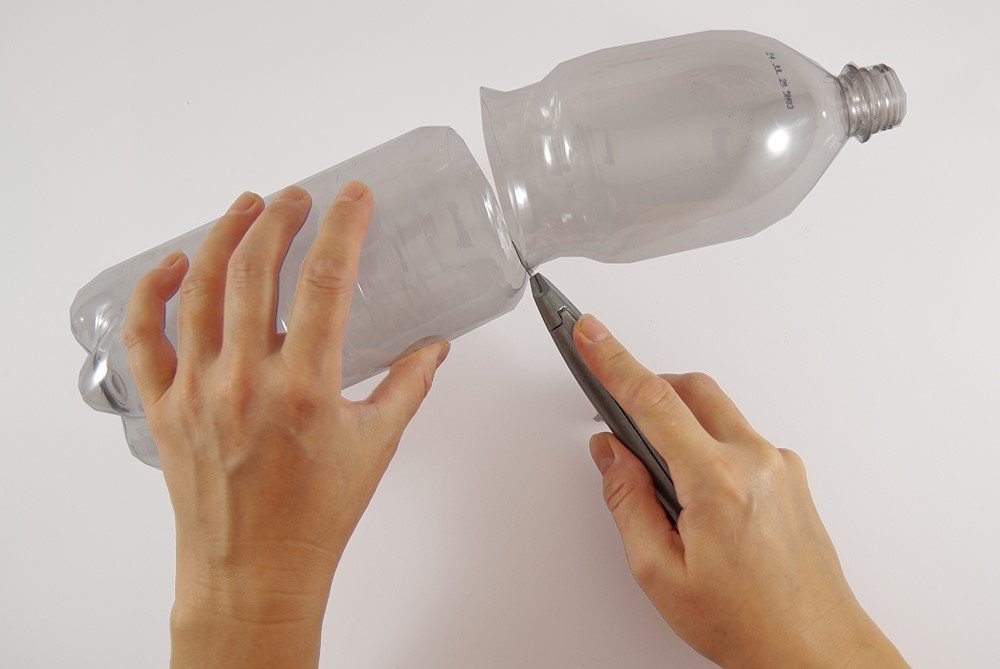 Eine Hand hält eine PET-Flasche. In der anderen Hand ist ein Cutter, der die Flasche halbiert.