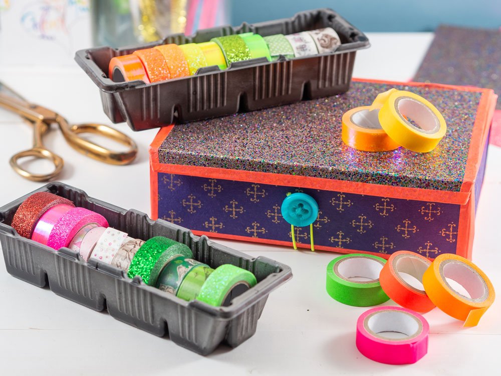 Washi-Tapes in leerer, bunt beklebter Keksbox, Schere und bunte Washi-Tapes auf Tisch