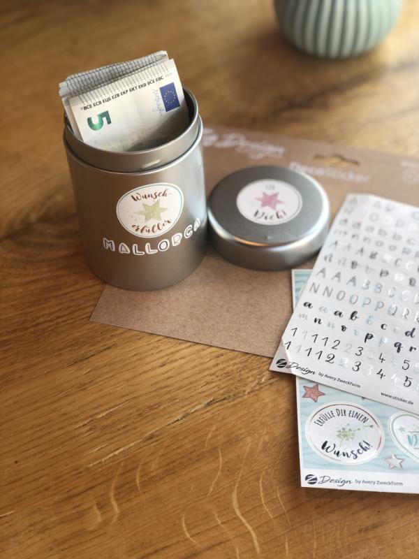 Eine Dose ist mit mehrern Stickern und dem Wort Mallorca beklebt. Darin stecken mehrere Geldscheine. Daneben liegen einige Stickerbögen.