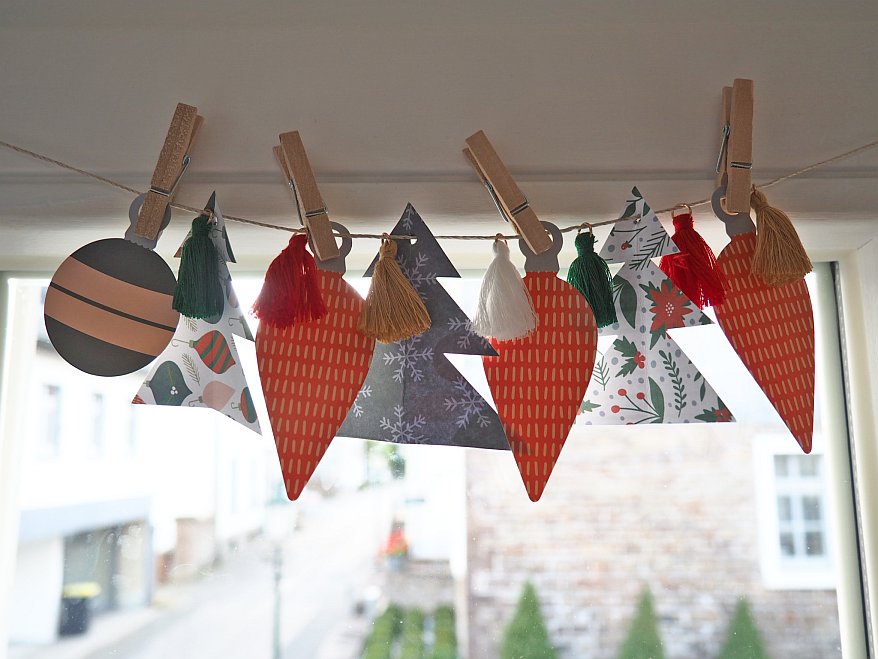 Weihnachtsgirlande aus Papier und Quasten, mit Klammern an einer Schnur befestigt.