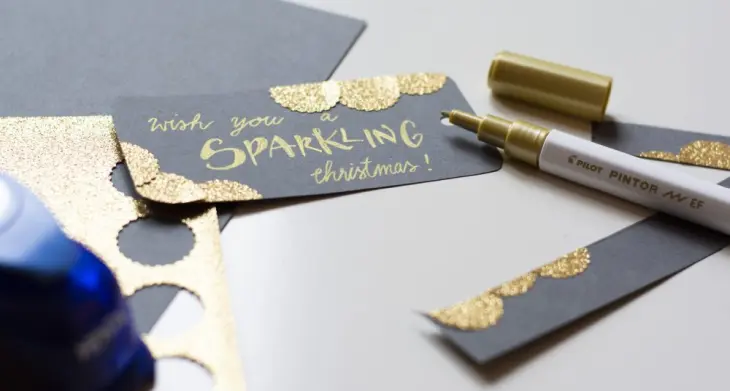 Detailaufnahme eines Geschenkanhängers zu Weihnachten. Auf grauem Papier steht in gold „Wish you a sparkling christmas!“ geschrieben. Daneben liegt ein Marker von PILOT.