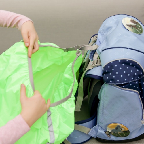 Zwei Hände stülpen ein Regencape über einen Schulranzen von ergobag.