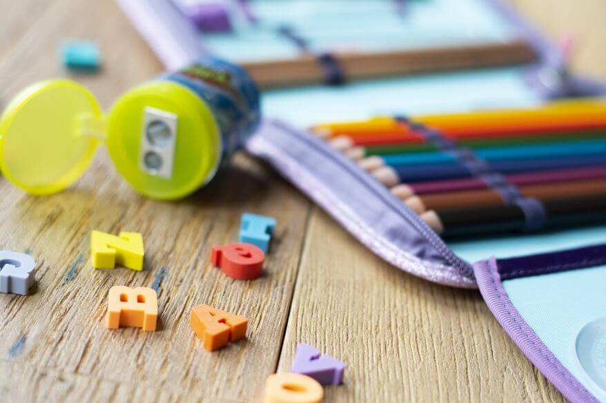 Nahaufnahme eines Schlumäppchens mit Stiften, Anspitzer und Radiergummi in ABC-Buchstabenform.