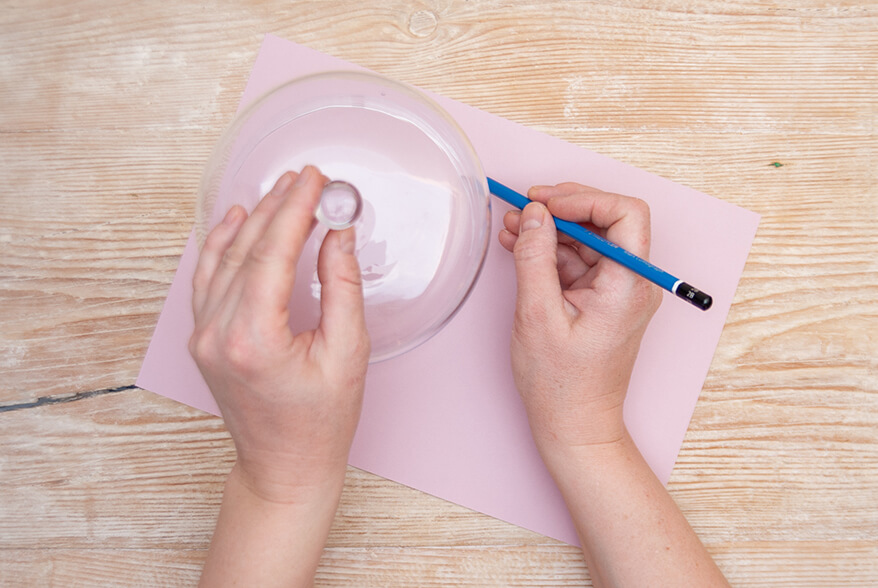 Auf einer hellen Holzoberfläche liegt ein Blatt rosafarbenes Tonpapier von Artoz. Jemand zeichnet mithilfe einer Glasglocke und eines Bleistifts einen Kreis darauf. Foto: Johanna Rundel