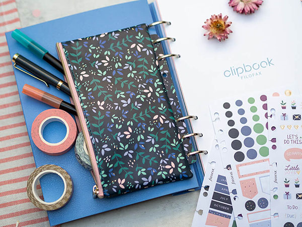 Auf einem hellgrauen Untergrund liegt ein aufgeschlagenes Clipbook von Filofax. Seitlich liegt ein eingeheftetes Etui, aus dem verschiedene Stifte und Washitapes herausschauen. Daneben sind ein paar Aufkleberbögen mit Stickern für ein Freundebuch zu sehen. Foto: Johanna Rundel