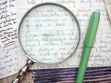 Auf einem dunklen, rustikalen Holztisch liegen verschiedene handschriftliche Briefe. Darauf eine Lupe, sowie ein hellgrüner Füller von Kaweco. Foto: Johanna Rundel