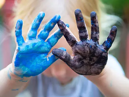 Ein Kindergartenkind hält beide Handflächen hoch, die rechte ist mit blauer Farbe, die linke mit schwarzer Farbe bemalt. Foto: Johanna Rundel