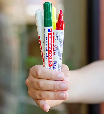 Jemand hält eine Hand voll edding-Kreidemarker in verschiedenen, weihnachtlichen Farben in die Kamera. Foto: Johanna Rundel