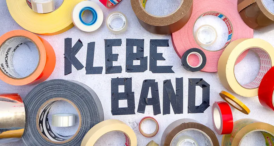 Um den, aus schwarzem Klebeband geklebten Schriftzug „Klebeband“, liegen viele bunte Rollen verschiedener Klebebänder. Foto: Johanna Rundel 