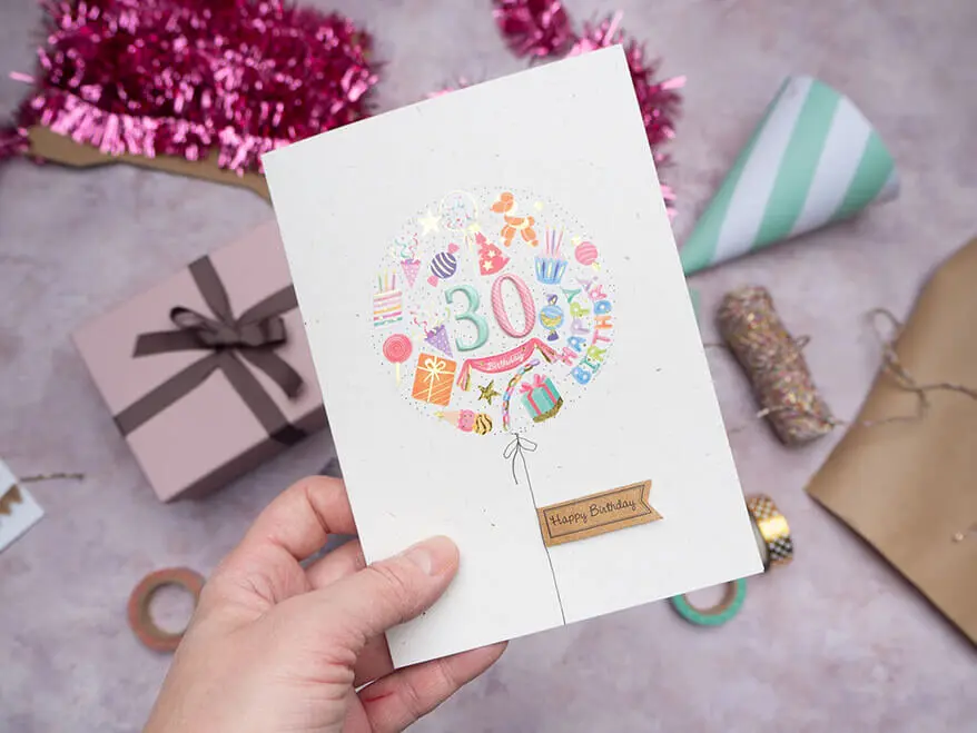 Jemand hält eine aus bunten Aufklebern von Rössler selbstgebastelte Glückwunschkarte zum 30. Geburtstag über einen rosa Untergrund. Foto: Johanna Rundel 