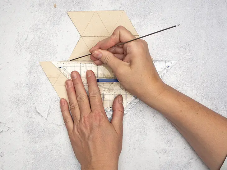 Jemand fährt Linien mit einer dünnen Stricknadel entlang eines geometrischen Musters auf einer Milchtüte nach.