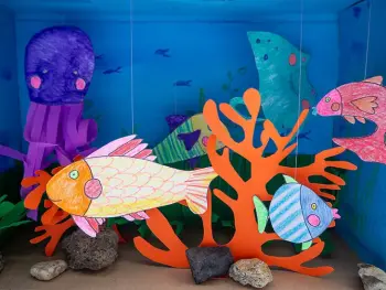 Nahaufnahme eines DIY-Aquariums aus einem Schuhkarton in dem bunt bemalte Fische aus Papier schwimmen. Foto: Johanna Rundel 