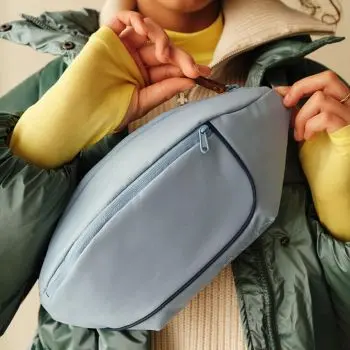 Ein Jugendlicher öffnet vor seiner Brust den Reißverschluss eines hellblauen Cross.Body-Bags von satch.
