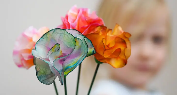 Ein Kind hält zwei bunte, selbstgebastelte Papierblumen aus Materialien von HEYDA und KNORR prandell, neben ihrem Gesicht. Foto: Johanna Rundel
