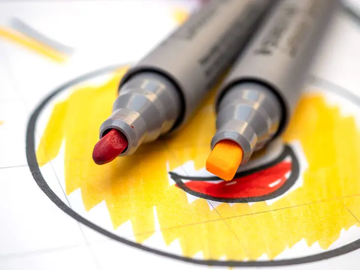 Ein roter Lumocolor Flipchartmarker von STAEDTLER mit Rundspitze liegt neben einem gelben mit Keilspitze auf einer gezeichneten Sonne. Foto: Johanna Rundel