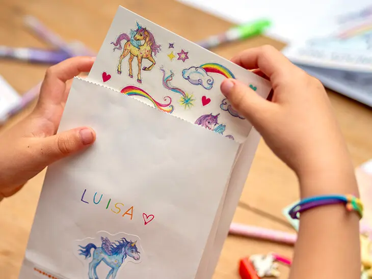 Ein Kind packt einen Bogen Einhorn-Tattoos von Coppenrath in eine selbstgestaltete Mitgebseltüte. Foto: Johanna Rundel