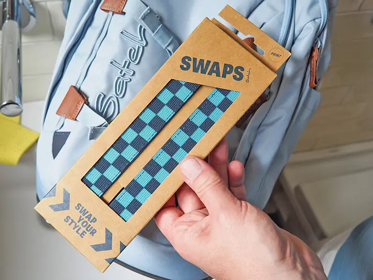 Jemand hält eine Packung blau-türkis gemusterte Swaps von satch über einen Schulrucksack, um sie auszutauschen. Foto: Johanna Rundel