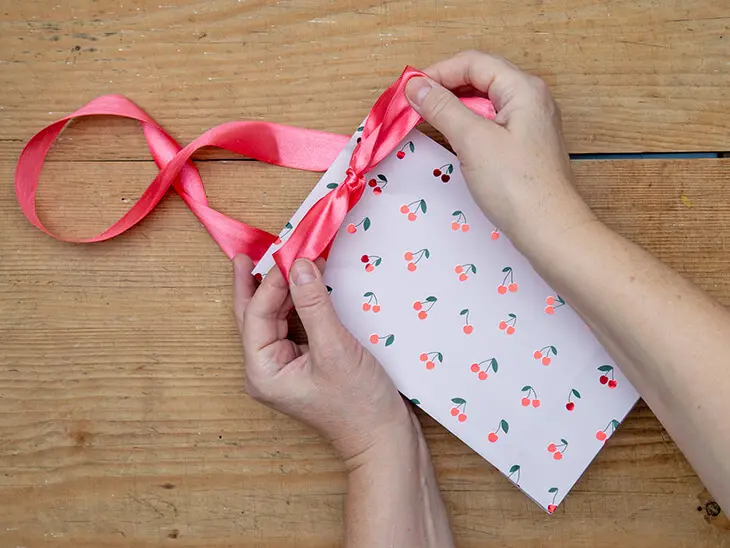 Jemand zieht ein Band durch ein Geschenktüte aus Geschenkpapier von STEWO. Foto: Johanna Rundel