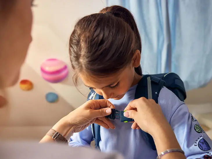 Eine Mutter stellt den Schulranzen ihrer Tochter ein.