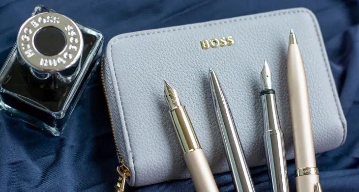 Zwei Füllhalter, zwei Kugelschreiber und ein Tintenfass von HUGO BOSS liegen auf blauem Satin