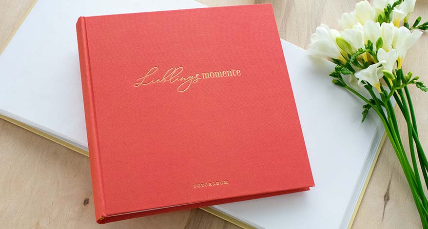 Ein rotes Fotoalbum auf einem Tisch, daneben liegen Blumen