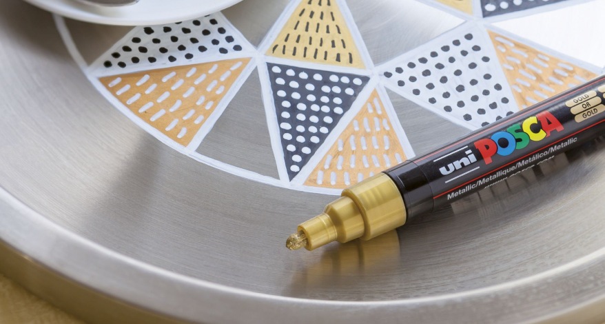 Goldener Posca-Marker verziert geometrisches Muster auf Metalltablett.
