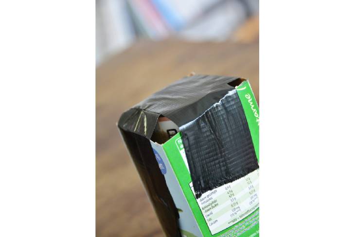 Nahaufnahme des Milchkartons, welcher mit einer Plastikflasche bestückt ist und mit schwarzem Panzertape zugeklebt ist.