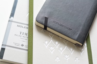 Drei edle Notizbücher, obenauf ein schwarzes Moleskine mit Gummiband.