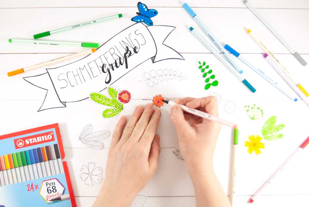 Hand malt Blumen neben Schriftzug „Schmetterlingsgrüße“ aus