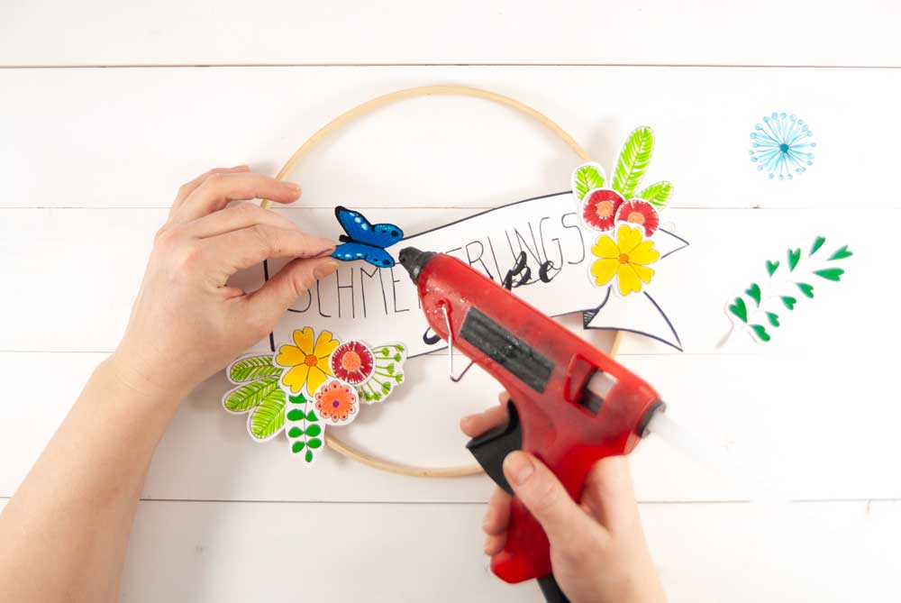 Hand befestigt Papier-Schmetterling mit Heißklebepistole auf Dekoreif