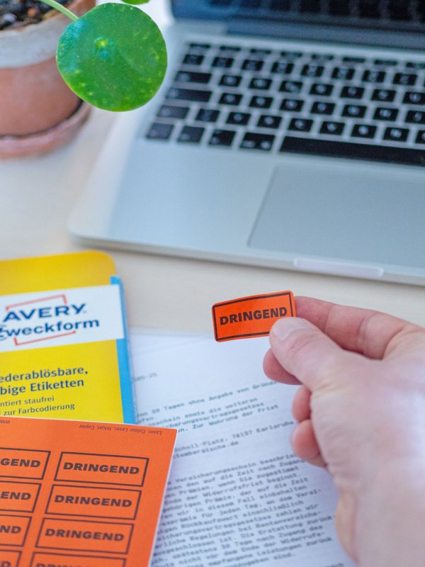 Etikett „DRINGEND“ wird vor Laptop auf Dokument geklebt.