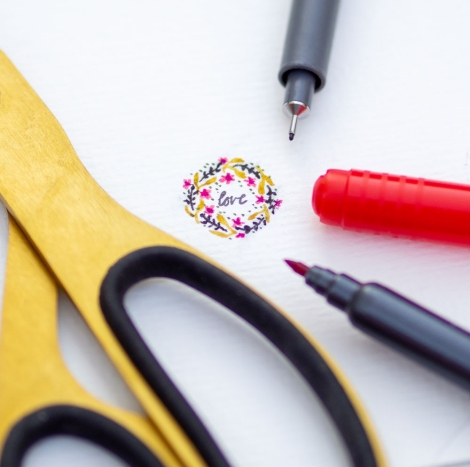„love“-Zeichnung inj der Größe eines 1-Cent Stücks, umrahmt von Stiften und Schere